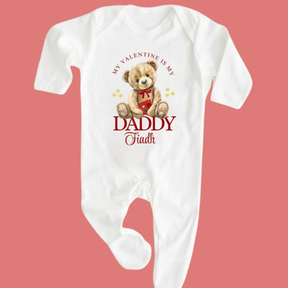 White baby onesie with teddy bear graphic and text on a pink background